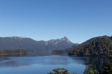 Etrafını çevreleyen ormanı ve Arjantin 'in Lago Espejo kentindeki sıradağları yansıtan devasa, berrak mavi bir gölün görkemli doğa görüntüsü.