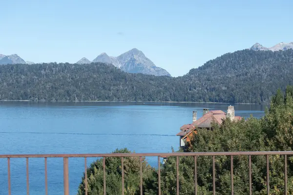 Dağ sıraları ve sık ormanlarla dolu mavi göl, ince ahşap parmaklıklarla balkondan manzara