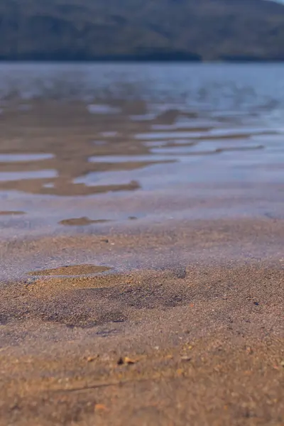 Kum tabanı olan bir gölde şeffaf su yansımalarının dikey yakın çekimi