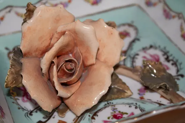 Kırılgan kadınsı açık deniz mavisi bir tabakta, parlak seramik pembe gül çiçeği ve ahşap bir arka planda çiçek süslemeleri.