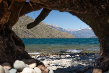 View of a lake with mountains behind from inside a tree bark in rocky ground in Lago Pueblo clipart
