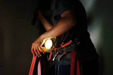 İnşaat işçisi, sahne ışığını kapalı alandaki iş yerinde kullanıyor. Işığı loş ışıklandırılmış çevre görüntüsü, güvenlik üzerine odaklanıyor.