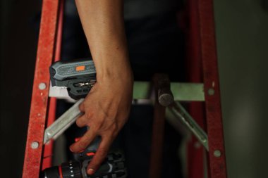 İnşaat işçisi, kapalı bir merdiven üzerinde elektrikli aletler kullanarak fotoğrafçılığı el pozisyonuna ve endüstriyel güvenliğe odaklıyor