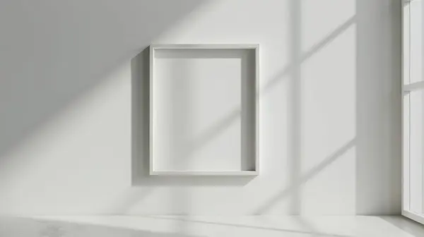 stock image A blank picture frame on a white wall, illuminated by natural sunlight streaming through a nearby window.