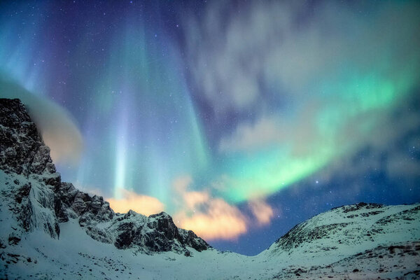 Ночью северное сияние со звездами над заснеженной горой на острове Лофотенбург, Норвегия