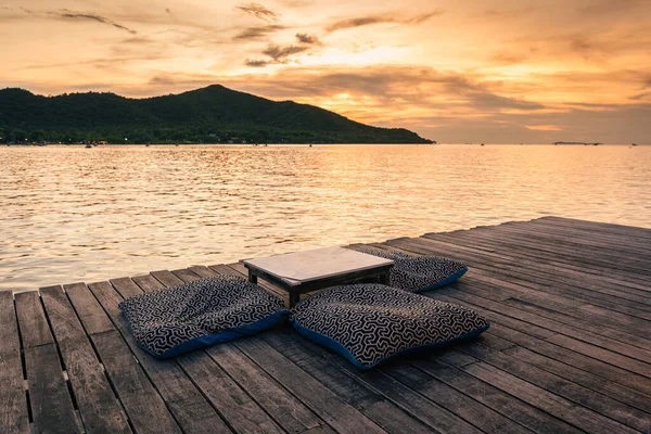 Seat cushion and table on wooden balcony by tropical sea in the evening