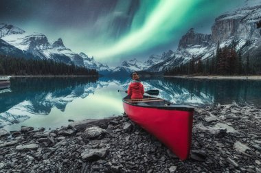 Aurora Borealis, Kanada, Jasper Ulusal Parkı 'ndaki Maligne Gölü' nde kırmızı kanoda oturan gezgin bayanla Spirit Adası üzerinde.