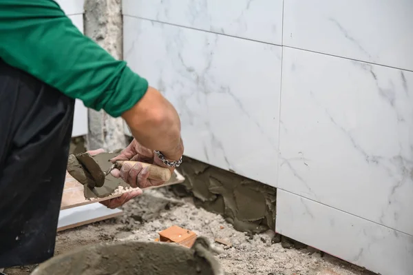 Male tiler using trowel laying marble tile with cement in bathroom. Housing development, Interior improvement renovation