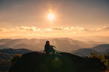 Başarılı bir siluet genç yürüyüşçü kadın ulusal parktaki dağın zirvesinde gün batımını seyrediyor ve dinleniyor.