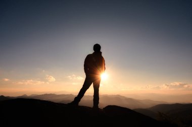 Başarılı bir genç yürüyüşçü dağın tepesinde güneşin batışında ulusal parkta duruyor.
