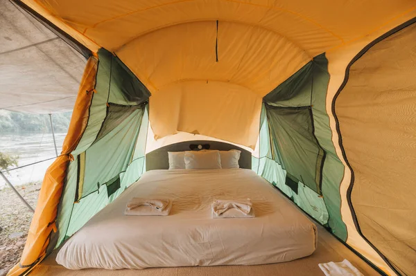 Inside of large comfortable camping tent on campground in the tropical forest by riverside on summer vacation
