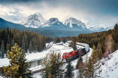 Morantlar Kavşağı 'nın manzarası ikonik kırmızı kargo treniyle kışın Kanada' nın Alberta eyaletindeki Banff Ulusal Parkı 'nda yay vadisi ve kayalık dağlardan geçiyor.