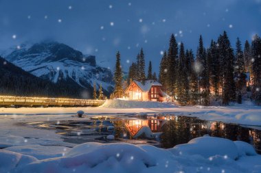Kanada 'nın Alberta kentindeki Yoho Milli Parkı' nda kışın çam ormanlarında parlayan ahşap kulübe ve kar yağışı ile Emerald Gölü 'nün güzel manzarası.