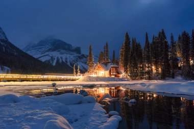 Kanada 'nın Alberta şehrindeki Yoho Ulusal Parkı' nda kışın karlı çam ormanlarında parlayan ahşap kulübesiyle Emerald Lake 'in güzel manzarası.