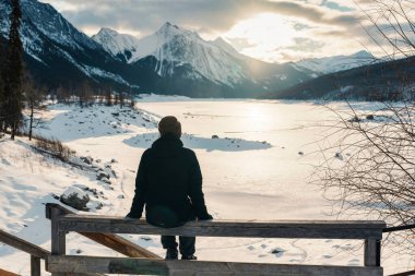 Seyyah 'ın kışın Medicine Gölü üzerinde gündoğumunun keyfini çıkarırken Jasper Ulusal Parkı, Alberta, Kanada