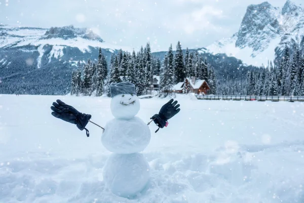 Happy snowman with beanie and glove in wintertime on wooden house village background in Emerald Lake. Merry Christmas and Happy New Year
