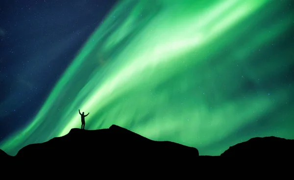 Successful silhouette mountaineer standing on top of mountain with Aurora Borealis glowing in the night sky on arctic circle at Scandinavia region