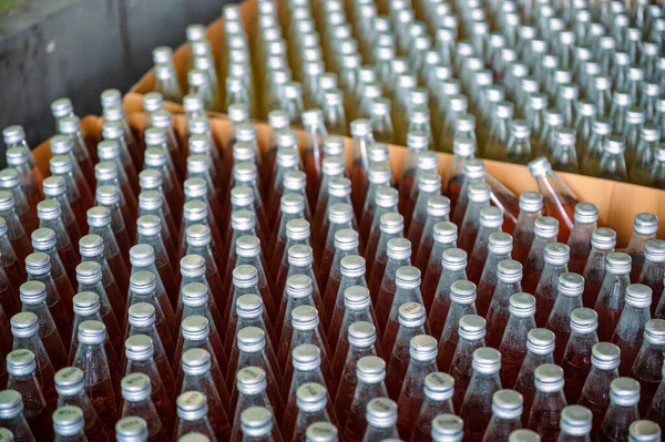 Group of red juice bottles with screw cap stacked in carton box for product export in warehouse at beverage processing plant