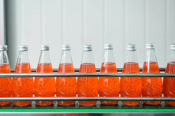 Automated production line of bottled juice beverage moving on conveyor belt in beverage processing factory