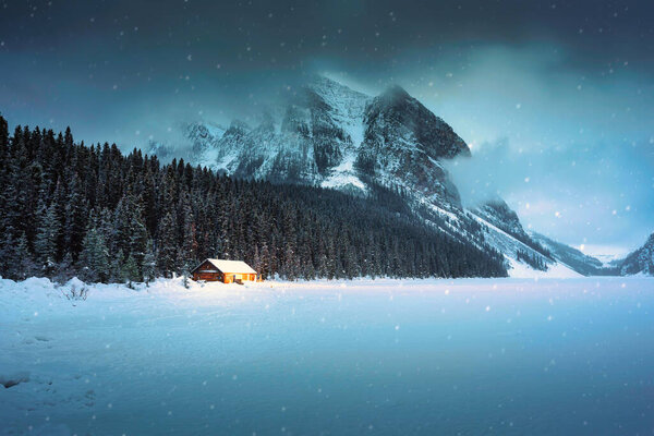 Beautiful scenery of Lake Louise with wooden cottage glowing and rocky mountains with snow covered in winter at Banff national park, Alberta, Canada
