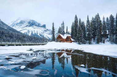 Donmuş Zümrüt Gölü 'nün güzel manzarası. Çam ormanlarındaki ahşap kulübe. Kışın Yoho Ulusal Parkı, Alberta, Kanada.