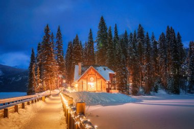 Kanada 'nın Alberta şehrindeki Yoho Ulusal Parkı' nda kışın karlı çam ormanlarında parlayan ahşap kulübesiyle Emerald Lake 'in güzel manzarası.