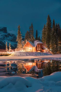 Kanada 'nın Alberta şehrindeki Yoho Ulusal Parkı' nda kışın karlı çam ormanlarında parlayan ahşap kulübesiyle Emerald Lake 'in güzel manzarası.