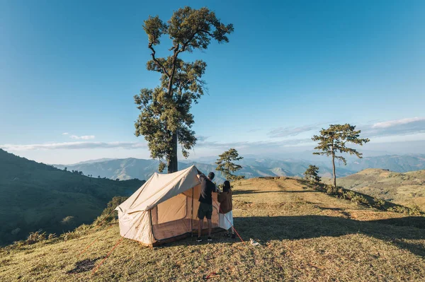 Young asian couple pitch a tent in campground on mountain hill in national park on summer vacation. Leisure activity and Recreational pursuit