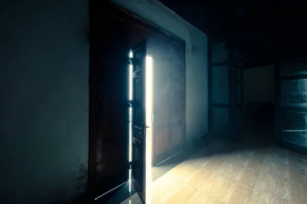 Wooden door opening with bright light shining in scary mystery darkness old room