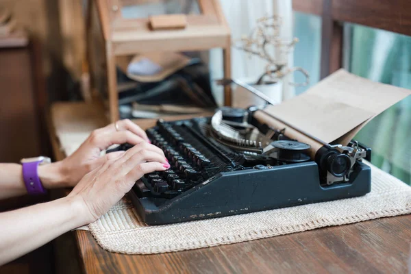 Hand of woman typing on old vintage typewriter with paper on wooden desk