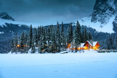 Kanada 'nın Alberta şehrindeki Yoho Ulusal Parkı' nda kışın karlı çam ormanlarında parlayan ahşap kulübesiyle Emerald Lake 'in güzel manzarası.