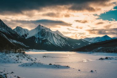 Jasper Ulusal Parkı, Alberta, Kanada 'da kayalık dağlar ve donmuş gölle birlikte Medicine Gölü' nün üzerinde güneşin doğuşunun güzel manzarası.