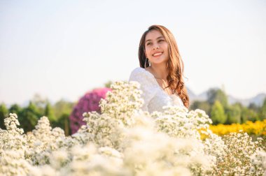  Mutlu, güzel Asyalı kadın, güneşli bir günde bahçede açan beyaz kesme çiçeğinin üzerinde durup gülümsüyor.