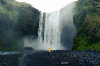 Skogafoss şelalesinin dramatik manzarası yaz mevsiminde İzlanda 'da Asyalı bir kadınla birlikte akıyor.