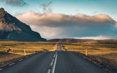 Manzaralı asfalt yol, güneş ışığı ve İzlanda 'nın yaz aylarında dağ manzarası.
