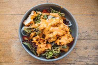 Kızarmış tavuk, marul karışık salata ve mayonez sosuyla ahşap masadaki seramik tabakta.