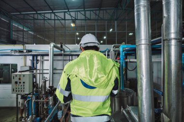Güvenlik üniformalı Kafkasyalı teknisyen boru hattında, içecek işleme fabrikasında kazan deposunda duruyor.