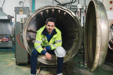 Güvenlik üniformalı mutlu beyaz mühendis endüstri imalat fabrikasında büyük bir kanal zıtlaşmasını işliyor ve rapor veriyor.