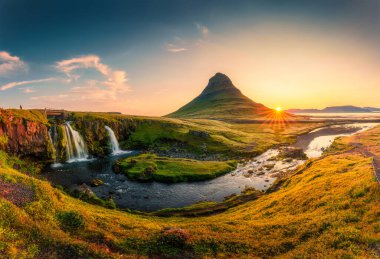 Kirkjufelfoss şelalesi ile birlikte İzlanda 'nın Snaefellsnes yarımadasında, Kirkjufell dağının tepesindeki gündoğumu manzarası