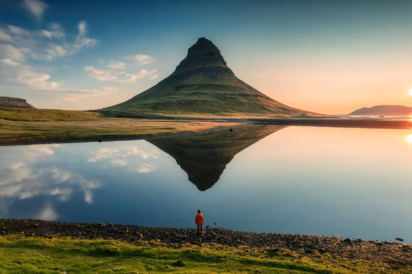 アイスランドのスナッフェルネス半島で夏の日の出の朝に湖の反射と男性の観光客が立っている雄大な対称性の火山カークファーフェル山の空中ビュー — ストック写真