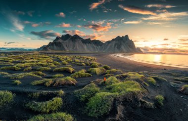 İzlanda 'nın güneydoğusunda Stoksnes yarımadasındaki siyah kumsalda çimen yığınıyla Vestrahorn dağının üzerinde güneşin doğuşunun güzel manzarası.