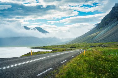 İzlanda 'nın güneşli bir gününde yol kenarından manzara, yol sisli vadi dağlarıyla dolu.