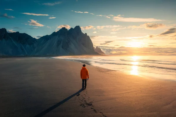 夏のアイスランドのストークスネス半島の黒い砂浜に立って日の出と男の間にベストラホーン山の息をのむような景色 — ストック写真