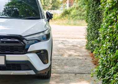 Bahçedeki bahçeye park edilmiş beyaz, modern bir SUV araba farının önünde.