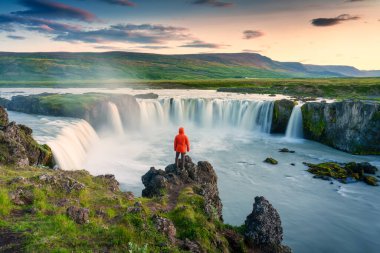 Godafoss şelalesinin görkemli manzarası. Renkli günbatımı gökyüzü ve erkek turist yaz mevsiminde Kuzey İzlanda 'da Skjalfandafljot nehrinin yamacında duruyor.