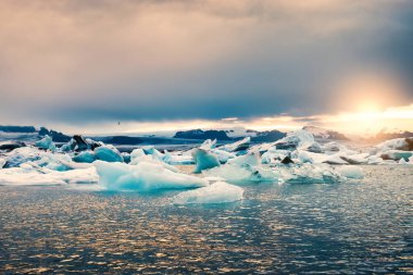 İzlanda 'daki Vatnajokull Ulusal Parkı' nda yaz mevsiminde eriyen mavi buzdağıyla Jokulsarlon buzulu gölünün üzerinde gün batımının güzel manzarası parlıyor.
