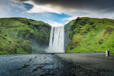 Güçlü Skogafoss şelalesinin heybetli şelalesi yazın İzlanda 'da keyif çatan çift turistle birlikte.