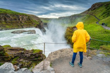 Sarı ceketli kadın turist Gullfoss Şelalesi 'nin ya da İzlanda' da yaz aylarında kanyonda akan aşırı Hvita nehri olan Golden Falls 'un manzarasının keyfini çıkarıyor.