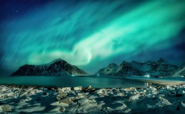 Aurora borealis 'in fantastik manzarası ya da Norveç' in Lofoten adaları Skagsanden Sahili 'ndeki Arktik Daire' deki karlı dağ sırasının üzerinde parlayan kuzey ışıkları.