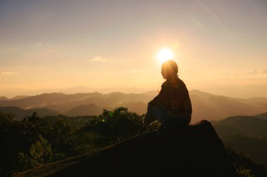 Başarılı bir siluet genç yürüyüşçü kadın ulusal parktaki dağın zirvesinde gün batımını seyrediyor ve dinleniyor.
